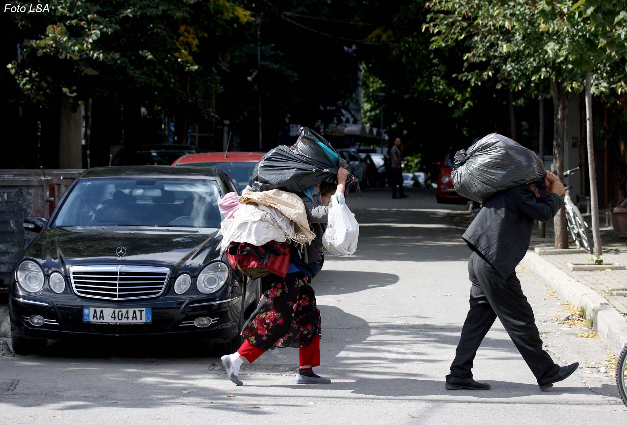 Nje cift te moshuarish, duke mbajtur ne krahe qese plastike te mbushura me rroba, prane rruges se Elbasanit./r/n/r/nA couple of elderly, by carrying the plastic bag filled with clothes, near Elbasan road.