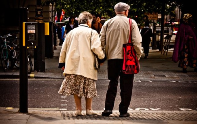 An elderly couple wait to cross the road